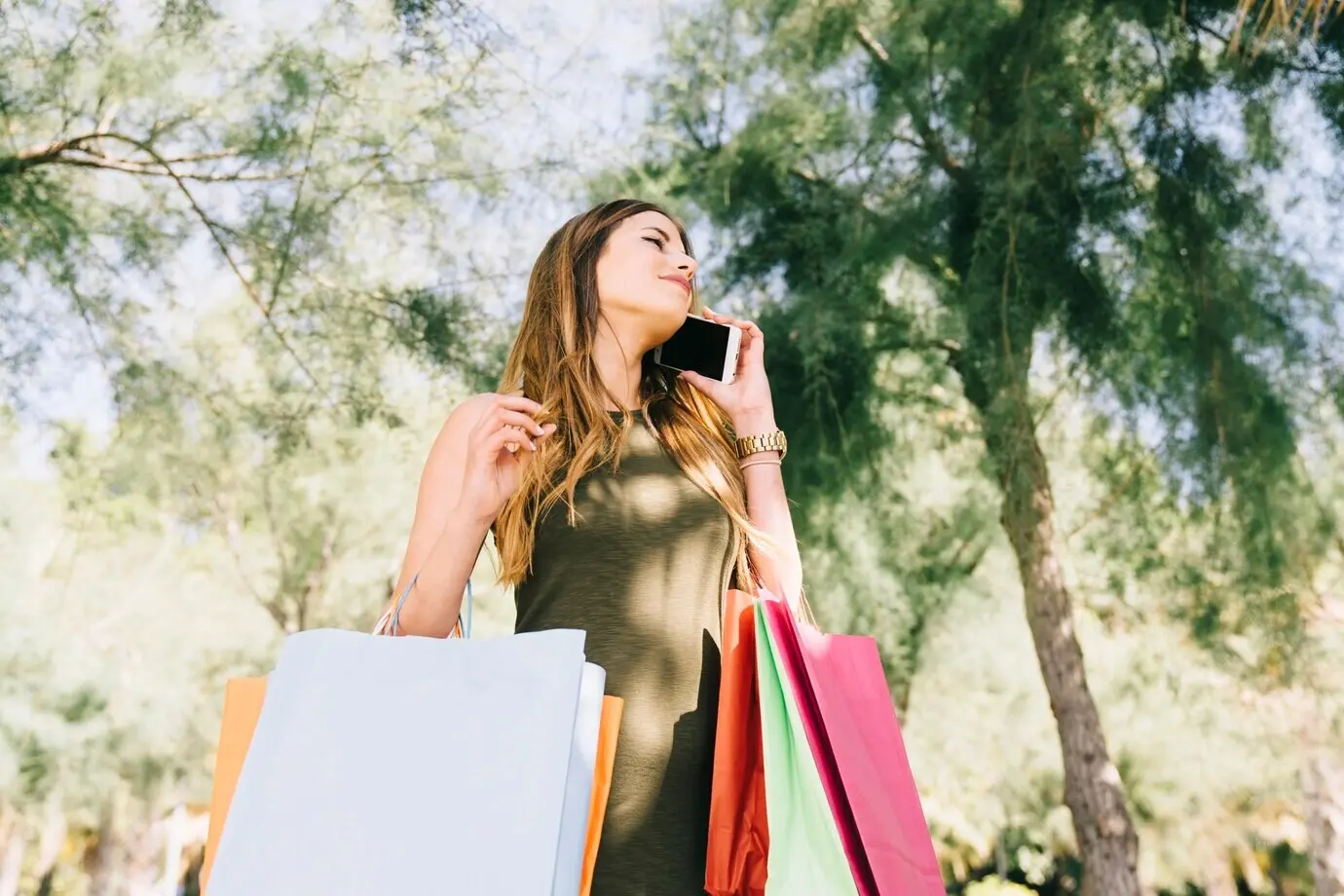 Mujer joven con bolsas de compras hablando por teléfono.